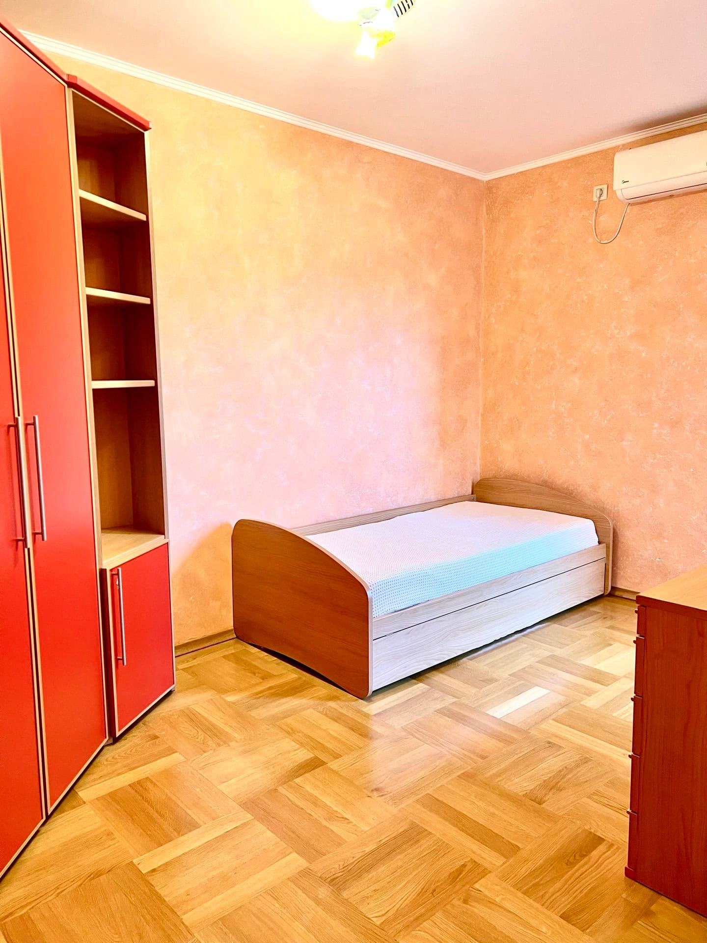 Chambre dans un appartement à Petrovac, Monténégro : lit simple, armoire rouge, parquet et climatiseur mural.
