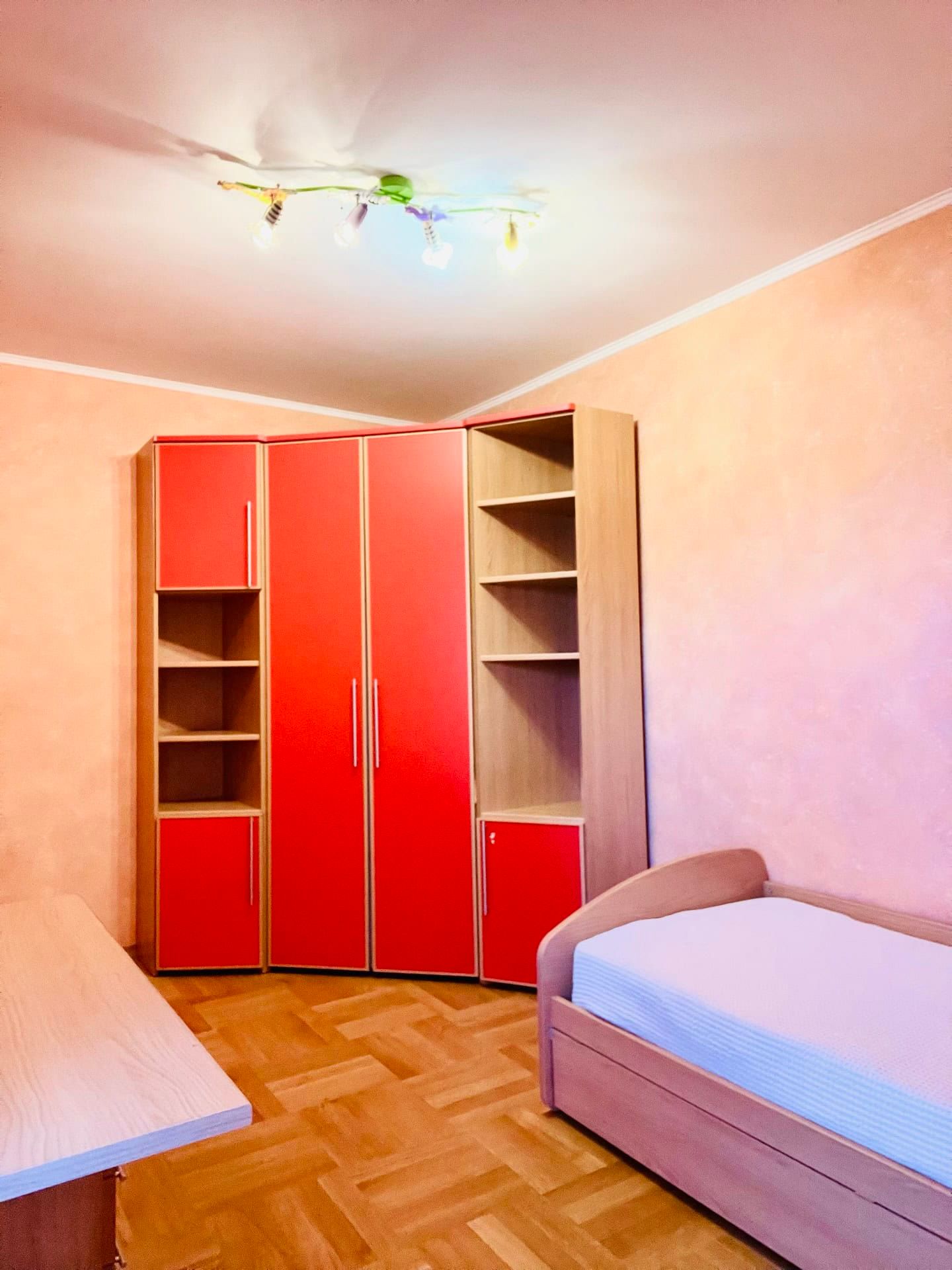 Chambre d’enfant avec une armoire rouge et un lit dans un appartement à Petrovac, Monténégro. Intérieur lumineux avec parquet.