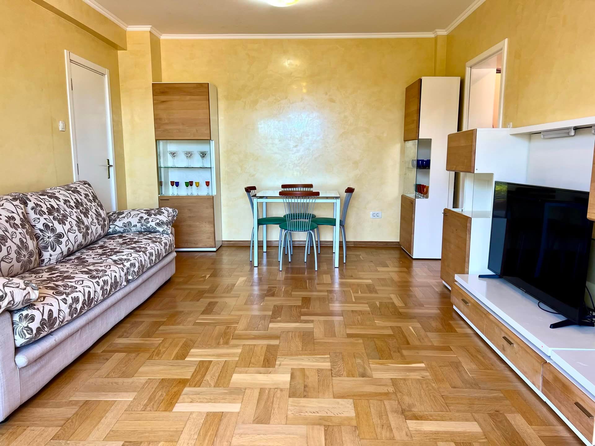 Salon dans un appartement à Petrovac, Monténégro : parquet, canapé moelleux, coin repas et meuble TV moderne.