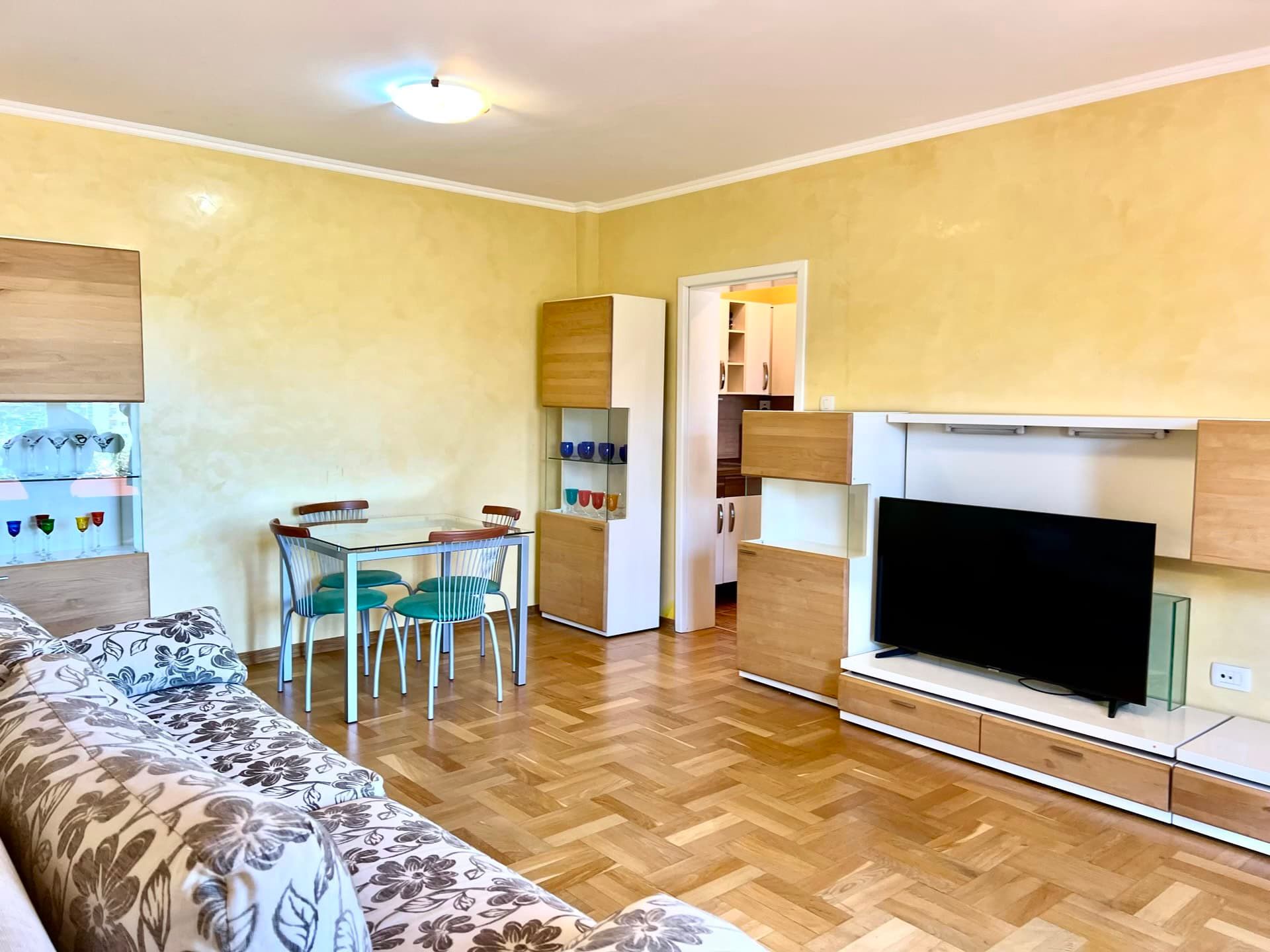 Salon avec parquet et coin repas dans un appartement à Petrovac, Monténégro : canapé moelleux, meuble TV et finitions claires.