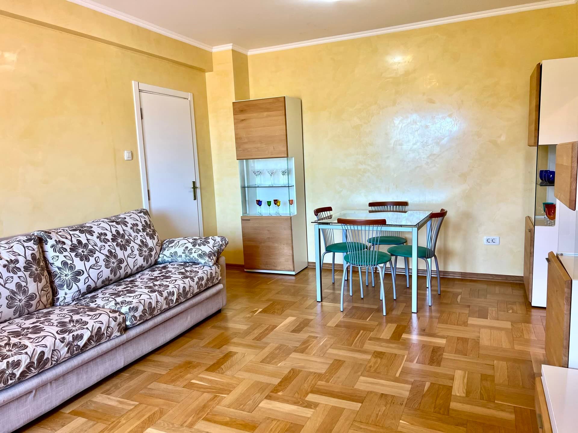 Salon dans un appartement à Petrovac, Monténégro : canapé à imprimé floral, coin repas et parquet.