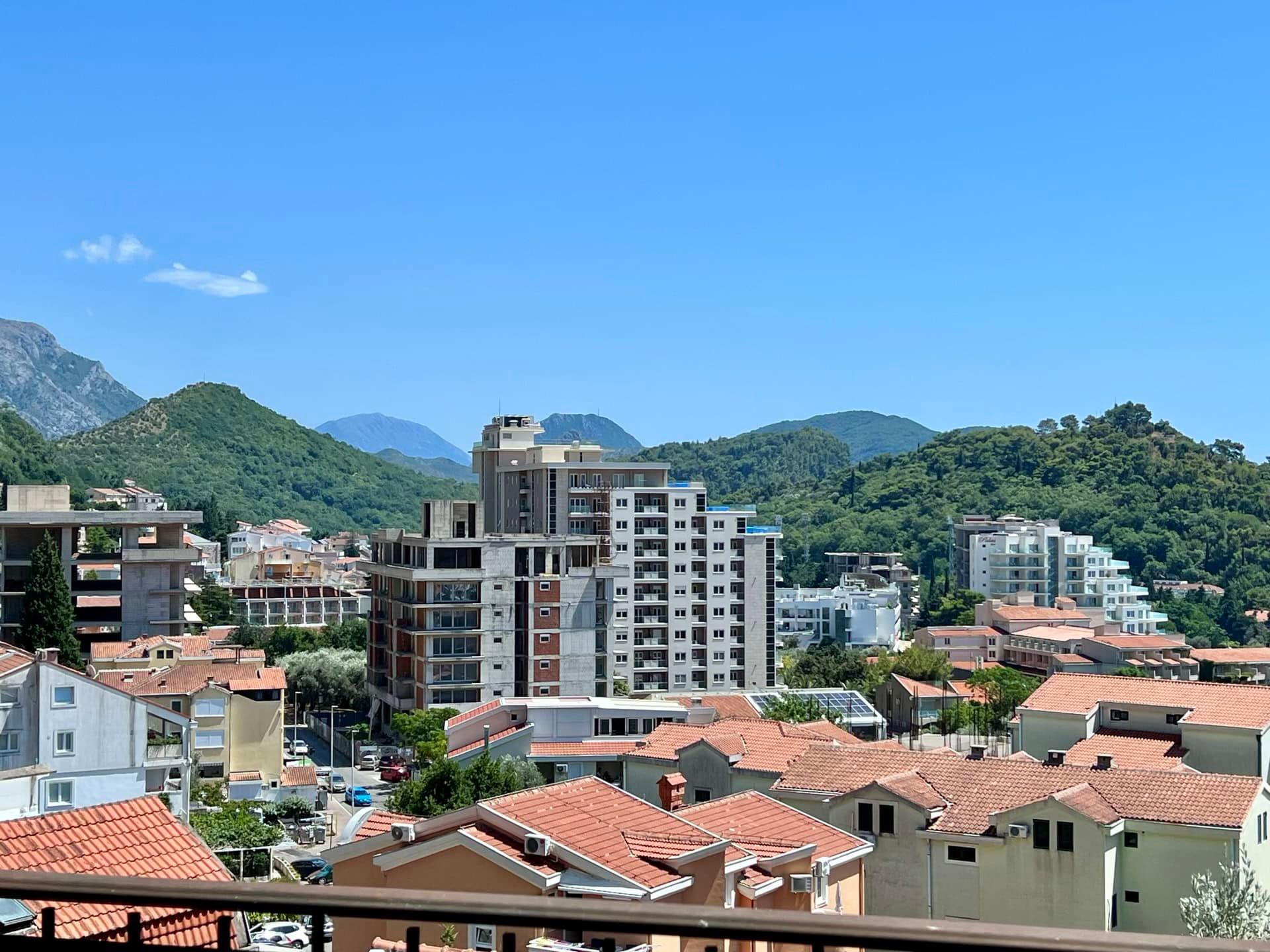 Vue panoramique sur la ville de Petrovac au Monténégro avec des immeubles résidentiels, des toits en tuiles et des montagnes verdoyantes en arrière-plan.
