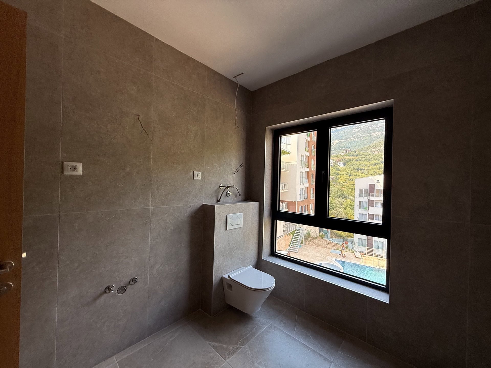 Modernes Badezimmer in einer Wohnung in Bečići, Montenegro: Fliesenverkleidung, wandhängendes WC und Blick auf den Pool.