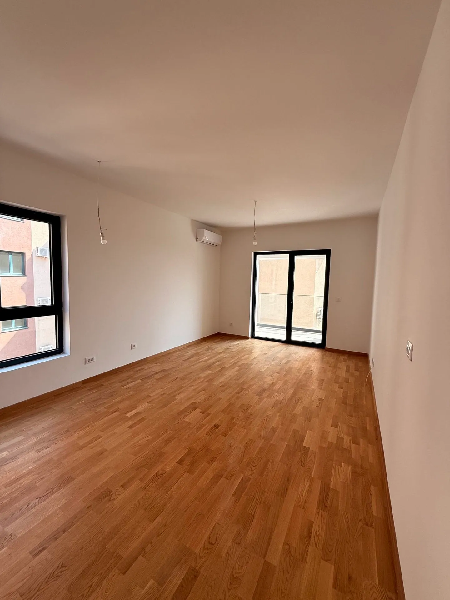 Ein leeres unmöbliertes Zimmer mit Holzboden, weißen Wänden und großen Fenstern.