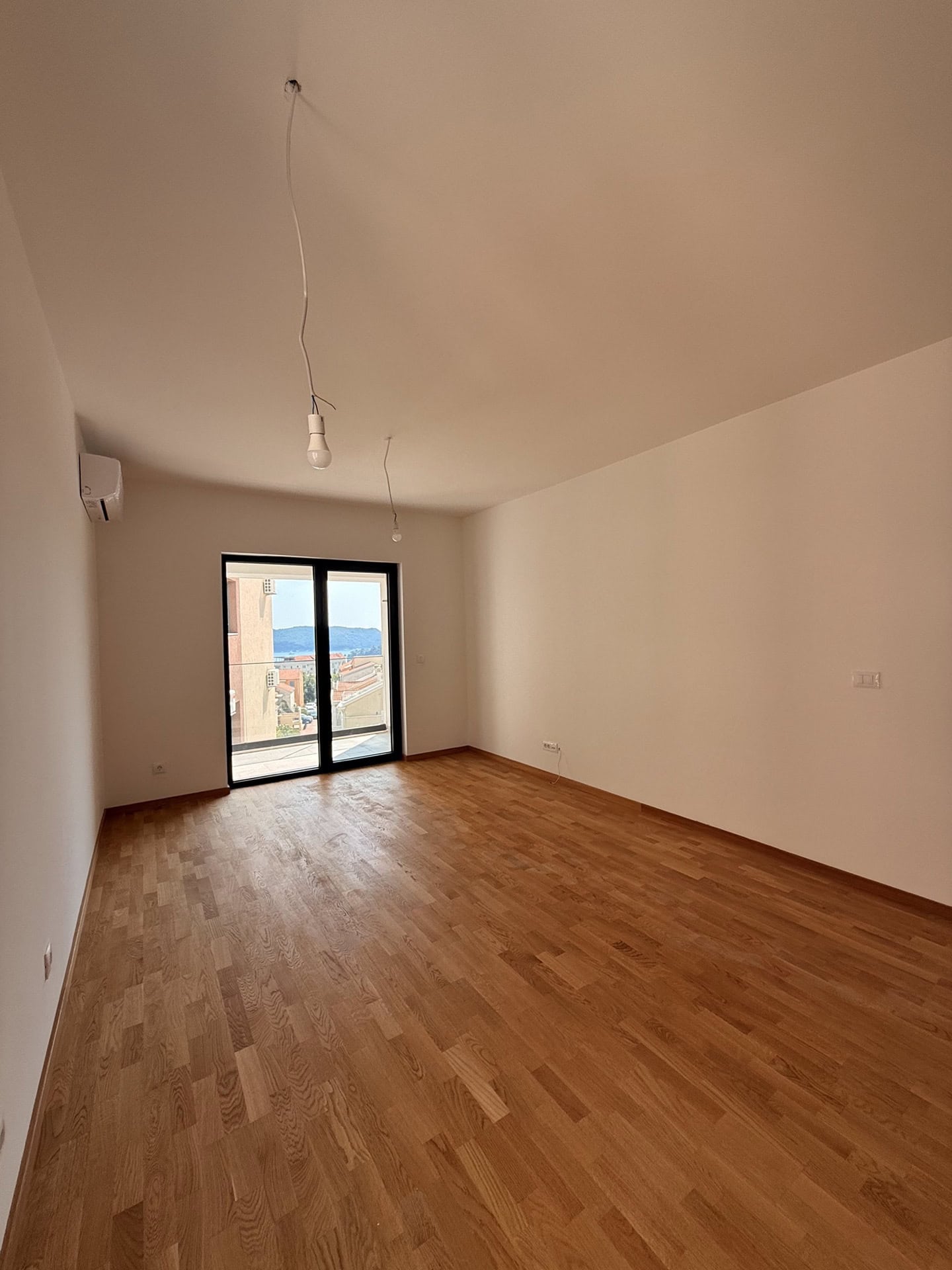 Helles Wohnzimmer mit Parkett und Zugang zum Balkon in einer neuen Wohnung in Bečići, Montenegro, mit Meer- und Bergblick.