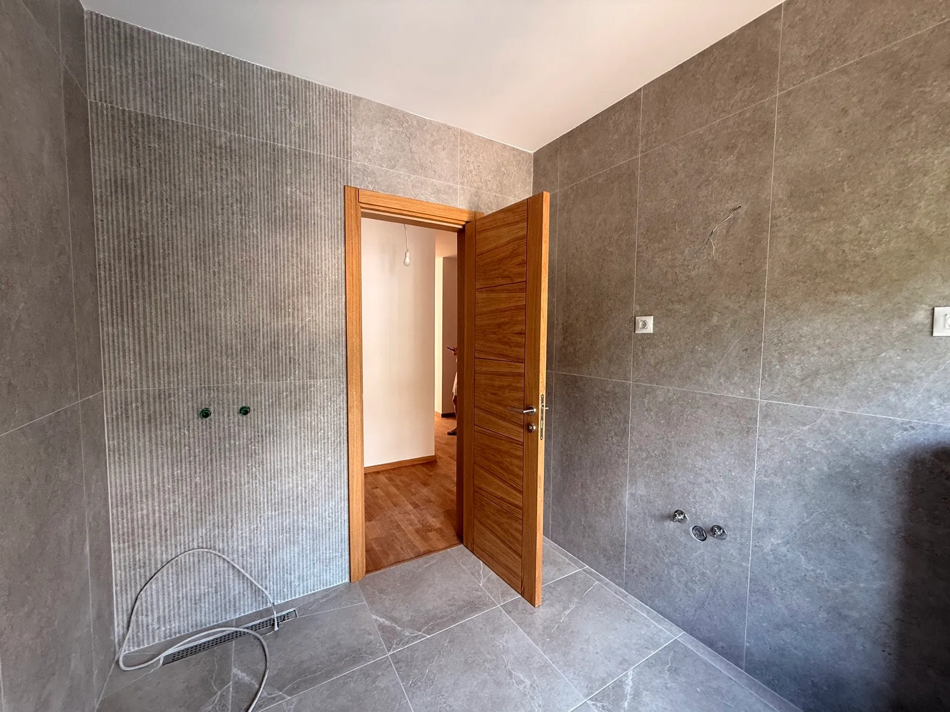 Ein teilfliesiertes Badezimmerinterieur mit Holztür und Wasserrohren.