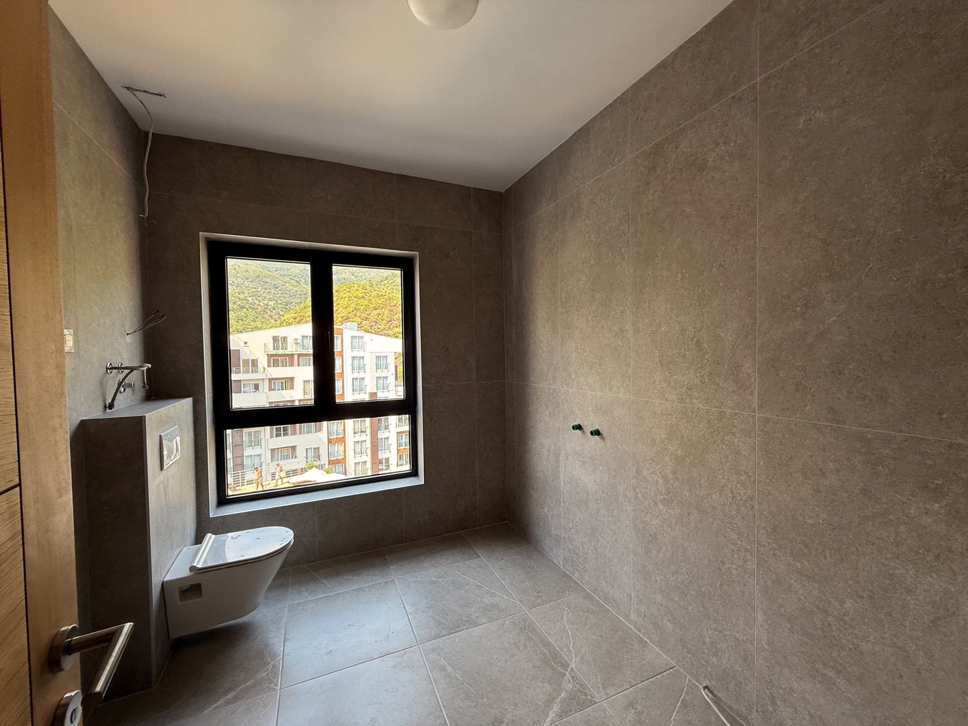 Modernes Badezimmer in einer Wohnung in Bečići, Montenegro: Fliesenverkleidung, Hänge-WC und Bergblick.