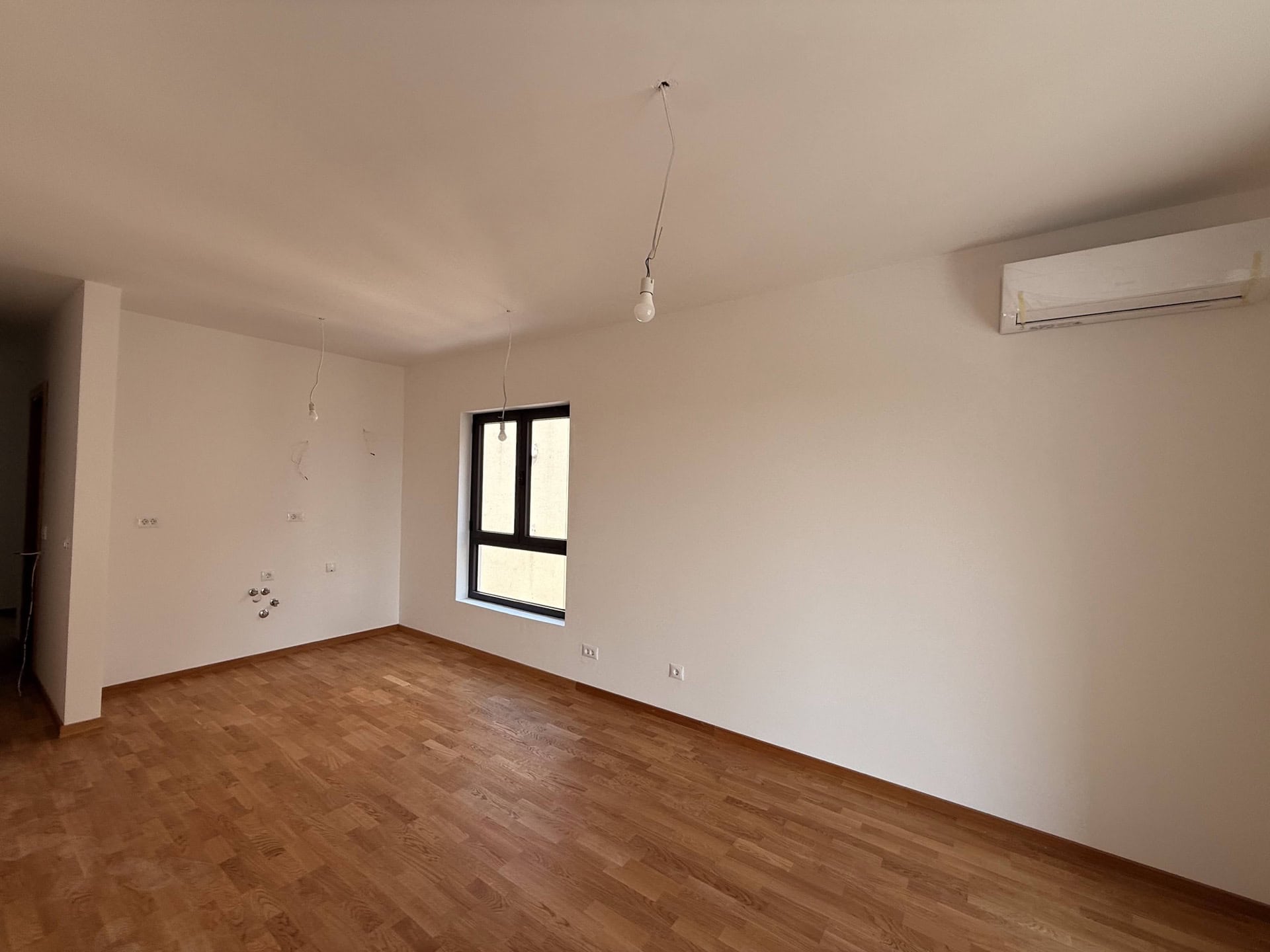 Helles Wohnzimmer in einem Neubau in Bečići, Montenegro: Parkettboden, weiße Wände, Klimaanlage und Panoramafenster.