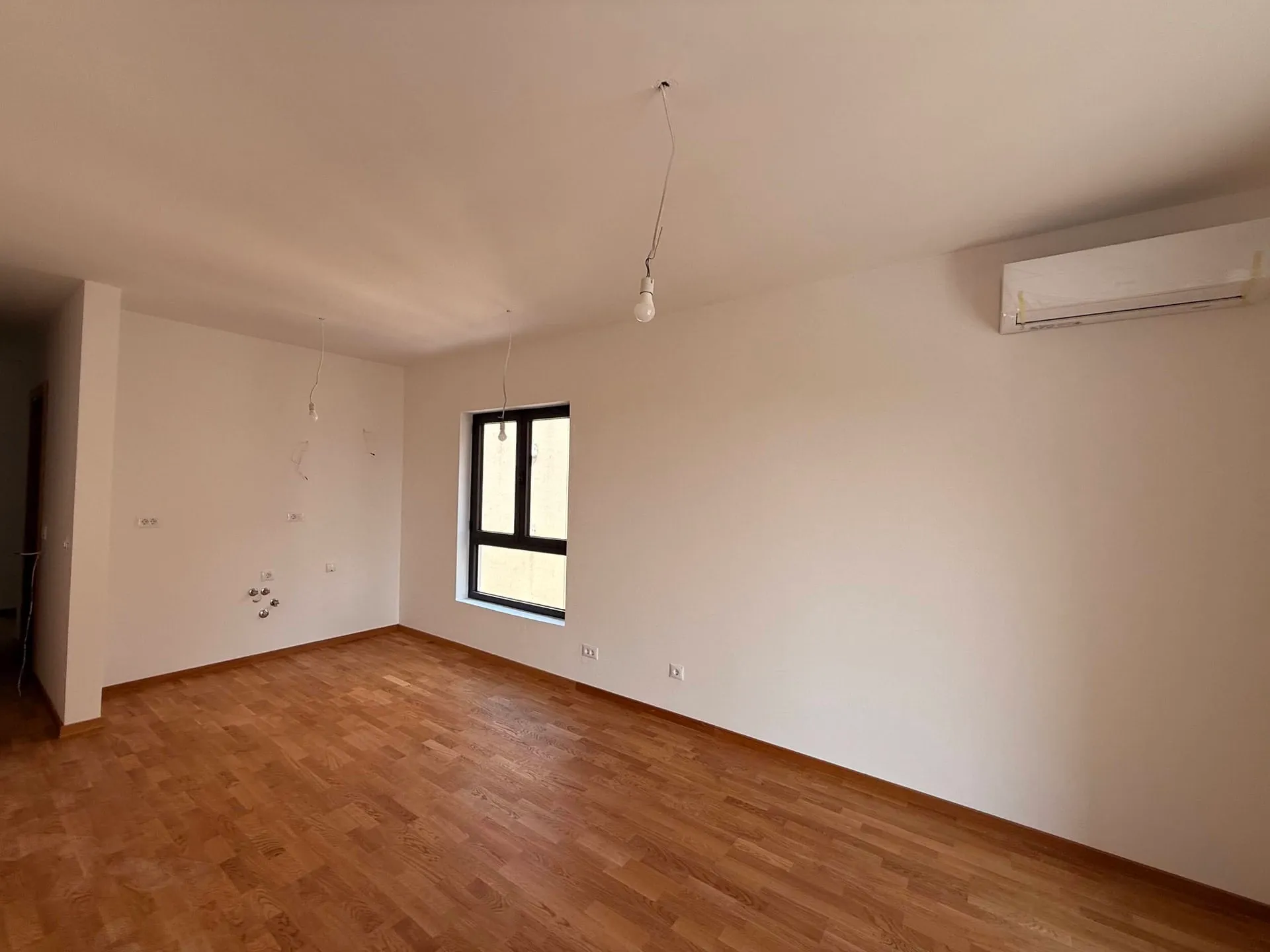 Leeres Zimmer mit Parkettboden und einem Fenster in hellen Farben