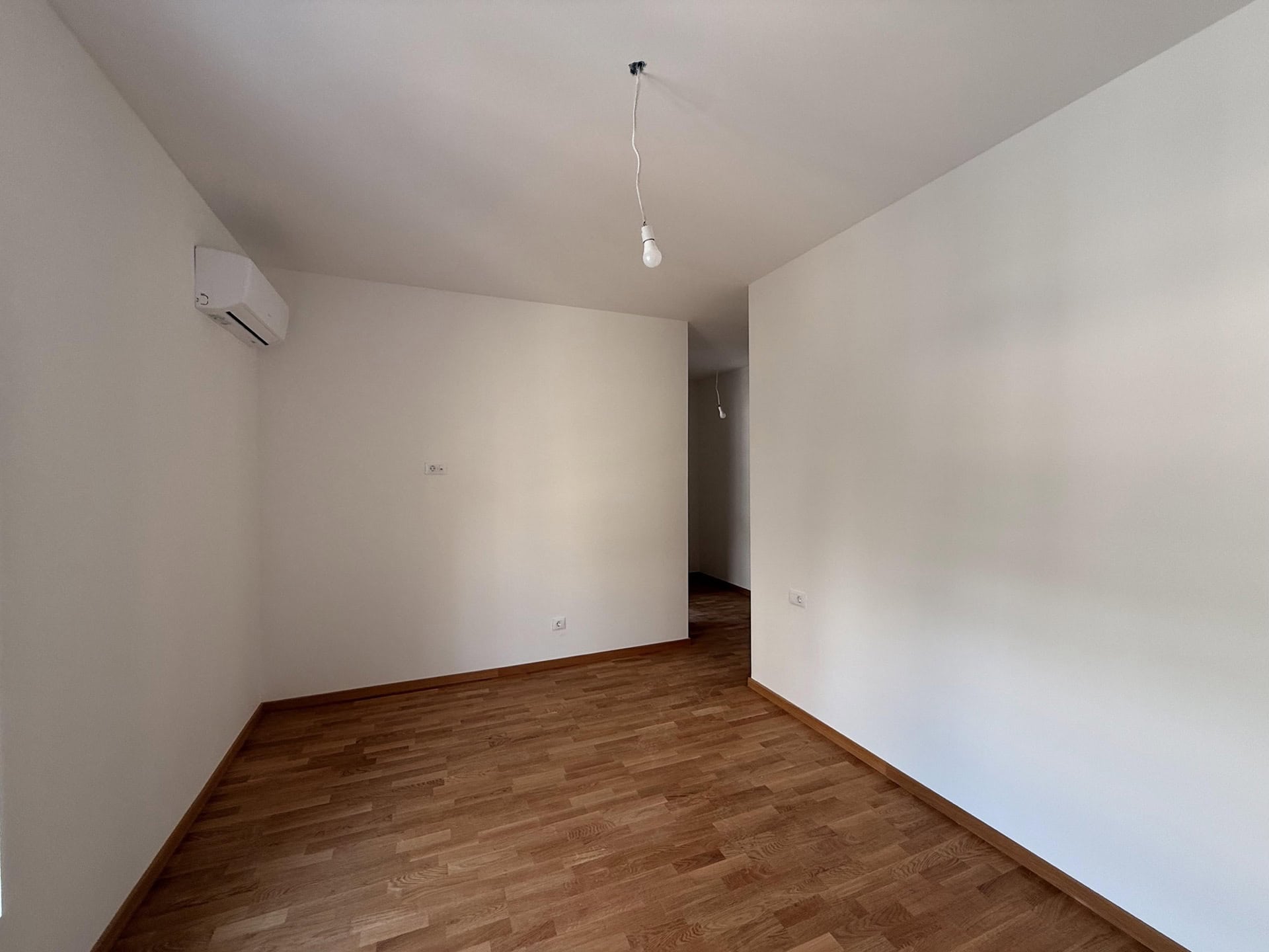 Helles Wohnzimmer in einer Wohnung in Bečići, Montenegro: weiße Wände, Parkettboden, Klimaanlage und Beleuchtung.