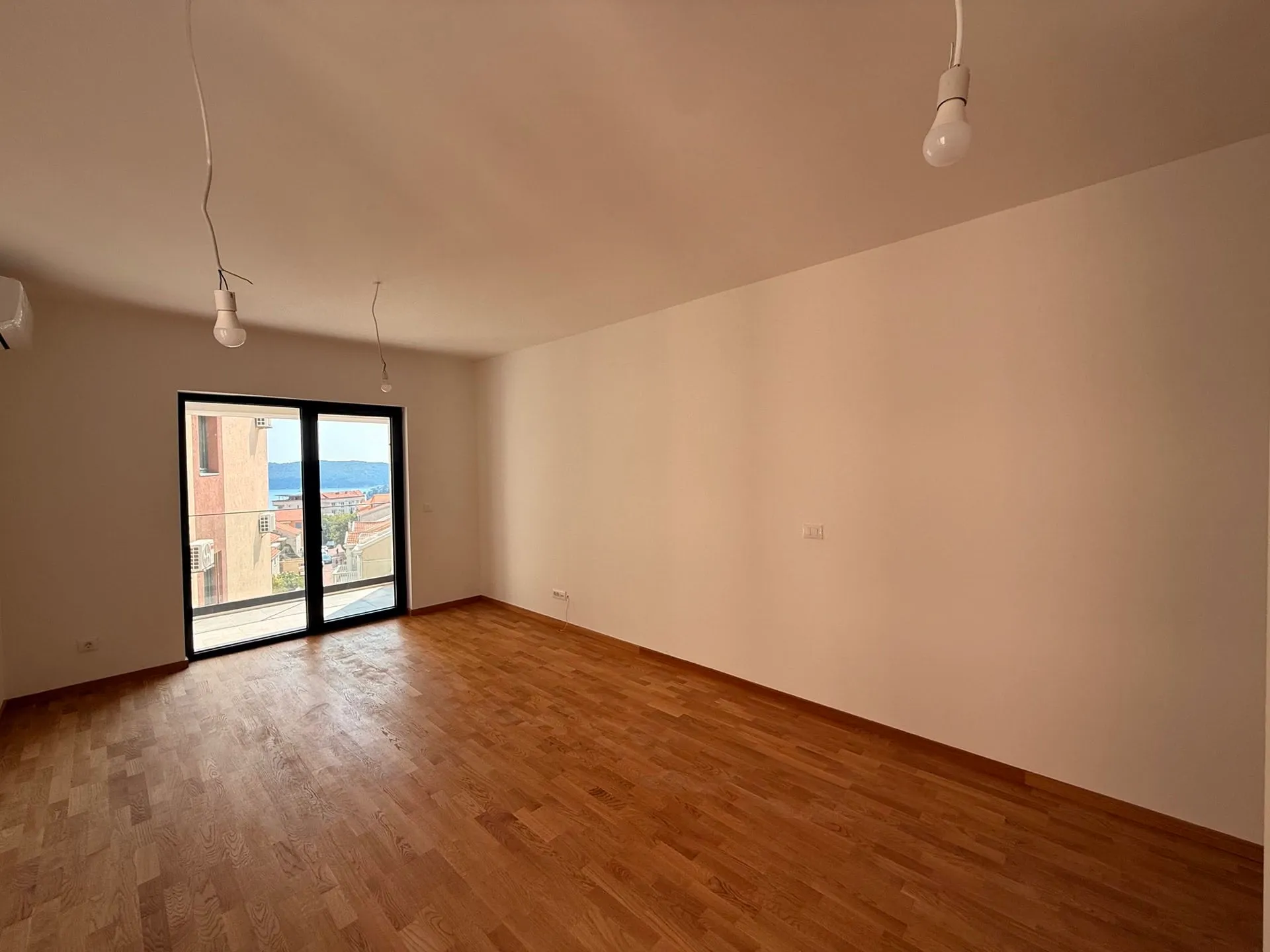 Ein leerer Raum mit Holzböden, weißen Wänden und einem großen Fenster.