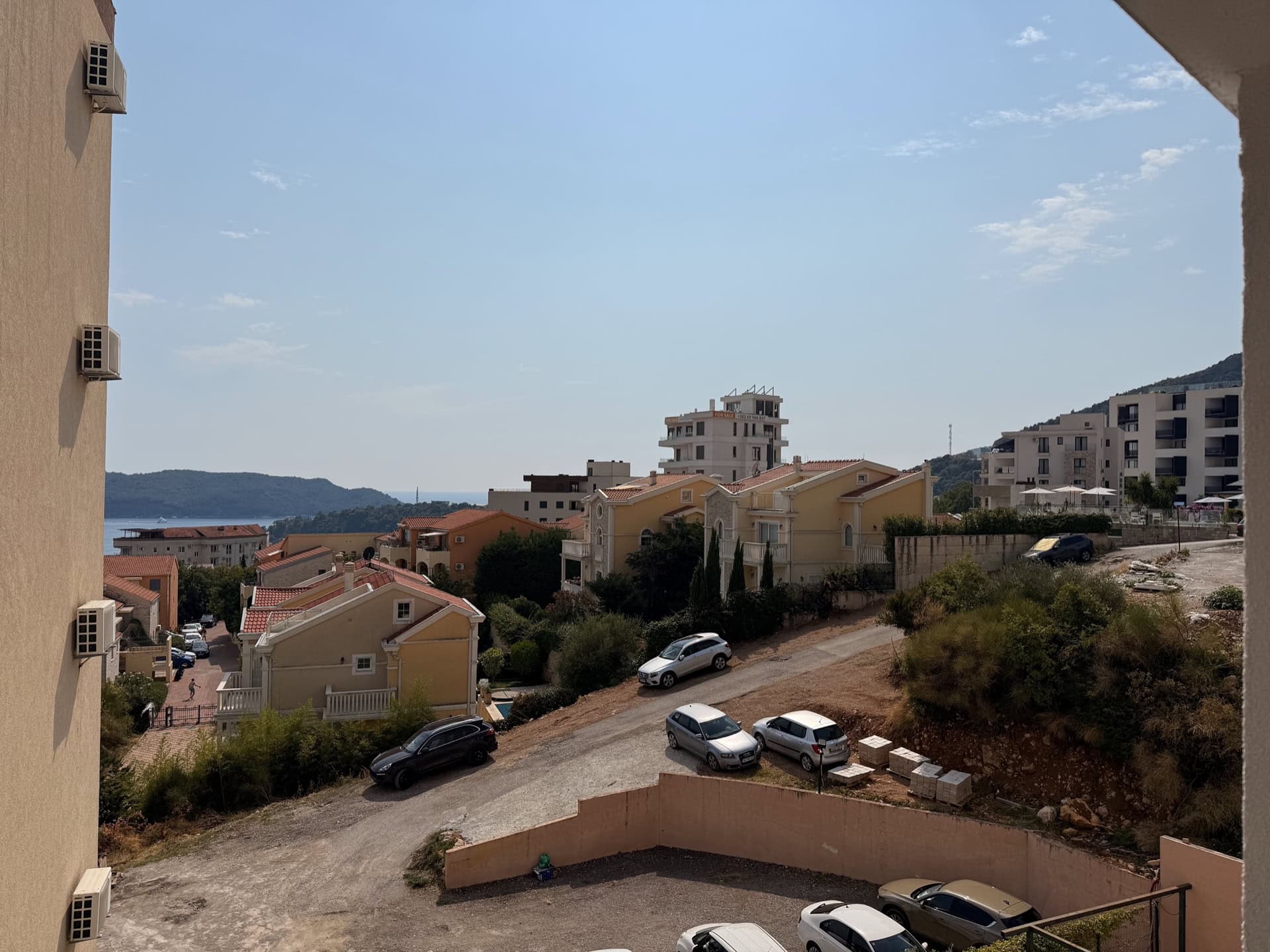 Blick vom Balkon der Wohnung in Bečići, Montenegro: Panorama auf die Wohnanlage, Berge und die Küste an einem sonnigen Tag.
