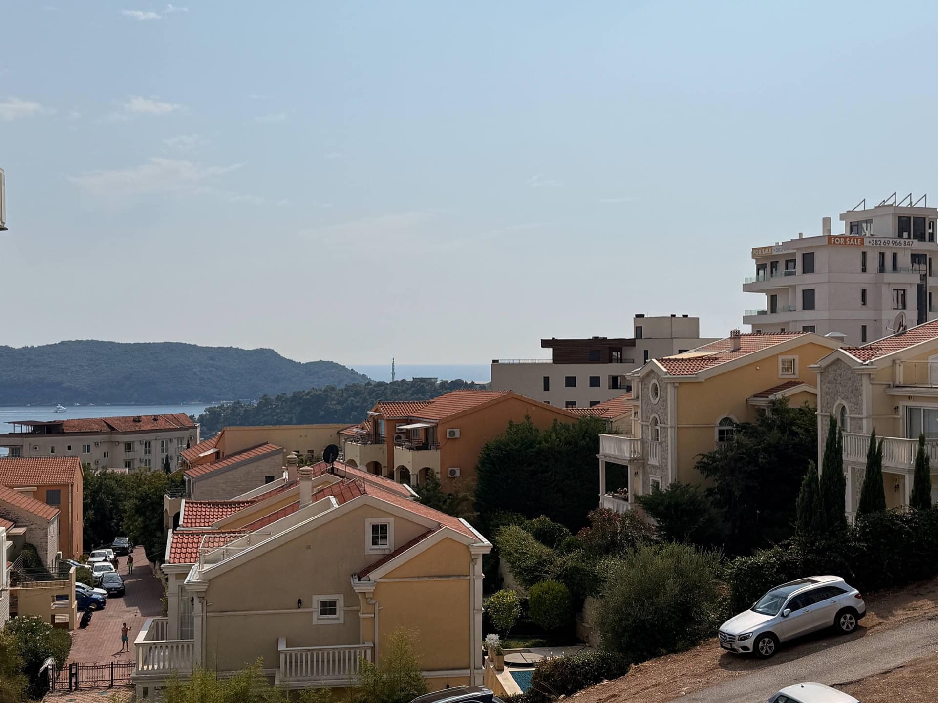 Panoramablick auf das Meer und die Wohnanlage in Bečići, Montenegro: gemütliche Häuser mit Ziegeldächern und grüne Hügel.
