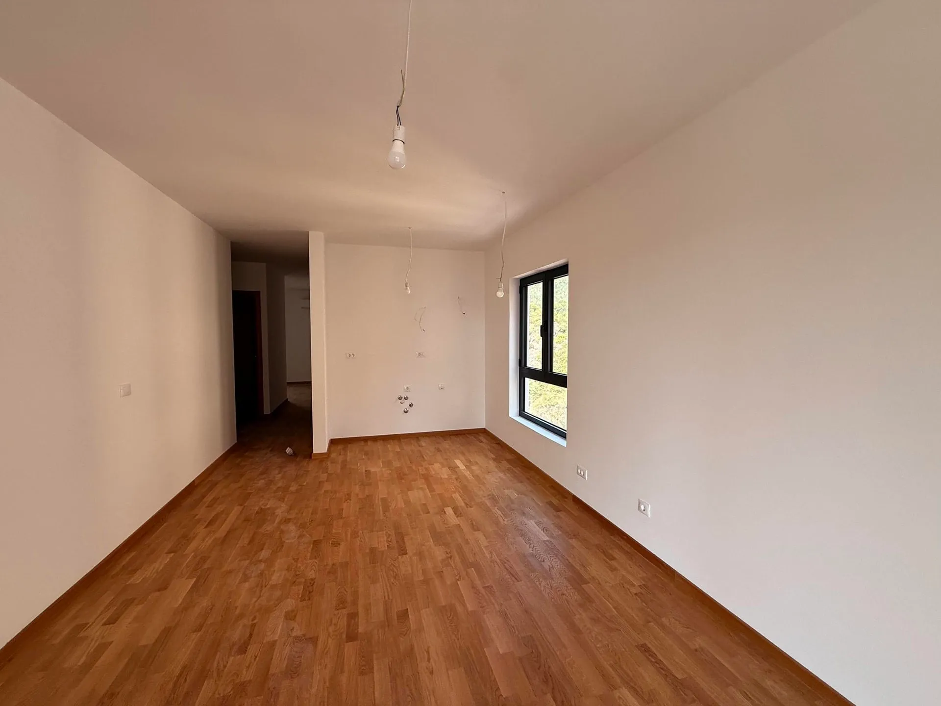Leeres Zimmer mit Holzboden und einem Fenster.