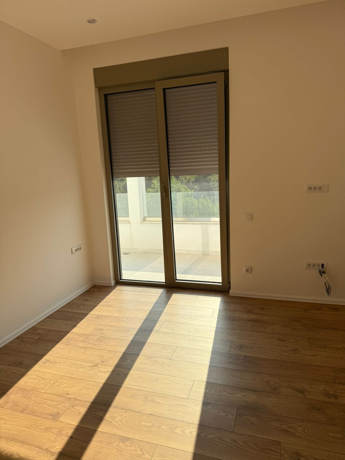 Helles Schlafzimmer in einem Neubau in Tivat, Montenegro: Laminat in Holzoptik, Panoramatür zur Terrasse und Rollläden.