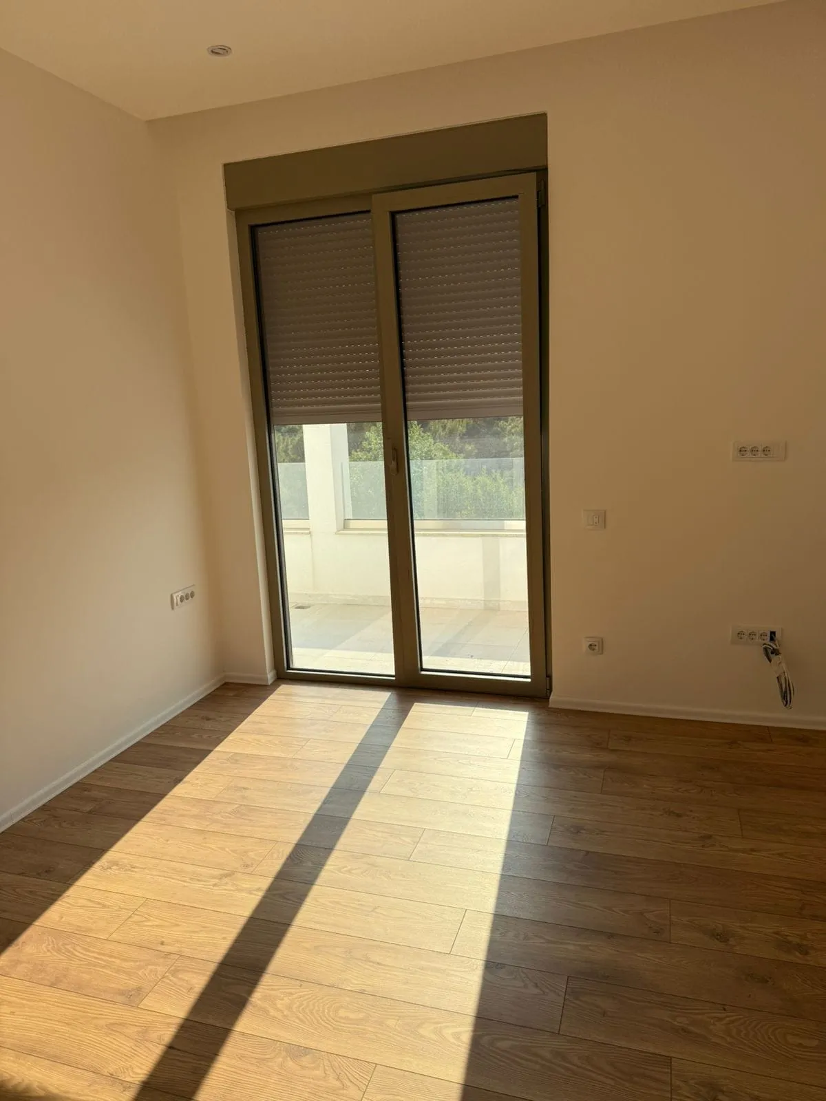 Bright bedroom in a new building in Tivat, Montenegro: wood-look laminate, panoramic door to the terrace, and roller shutters.
