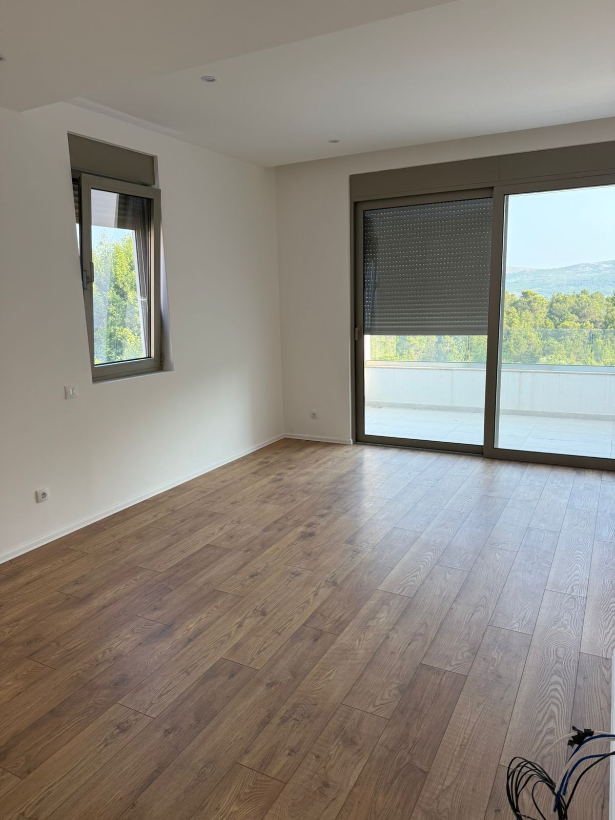 Helles Wohnzimmer in einer neuen Wohnung in Tivat, Montenegro: Laminat in Holzoptik, Panoramafenster und Zugang zur Terrasse.