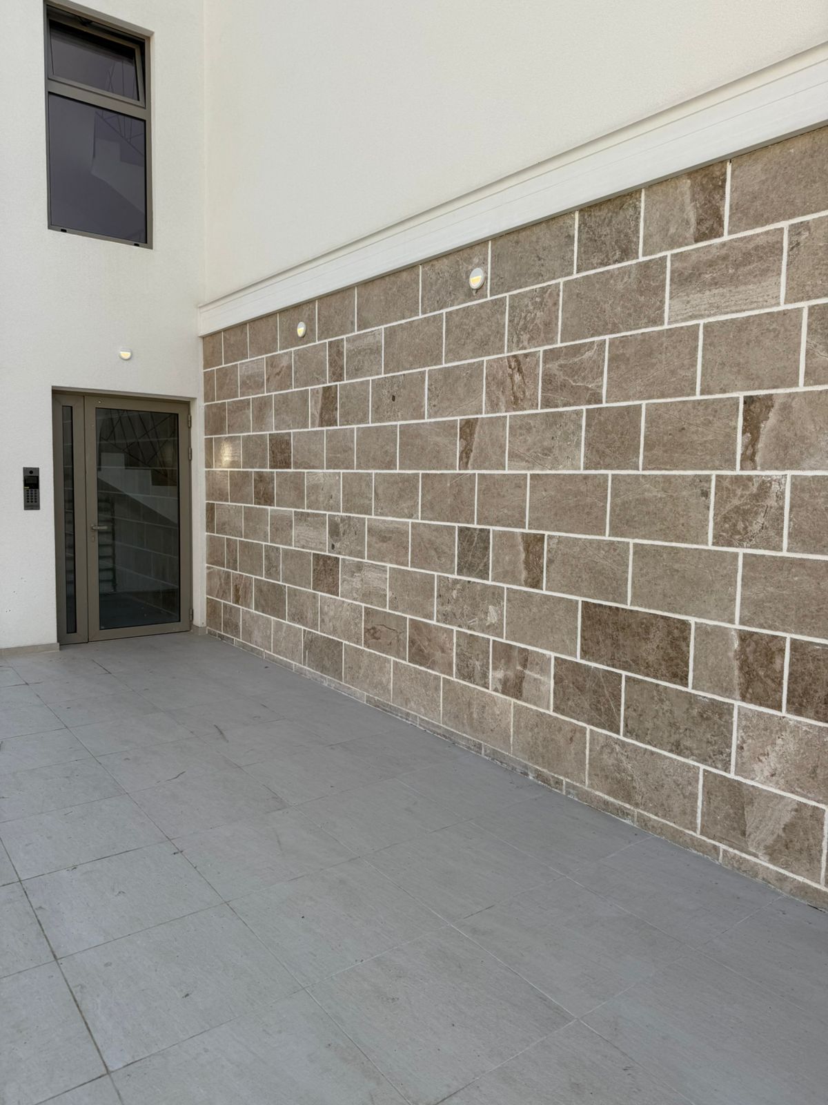 Fassade eines modernen Wohnhauses in Tivat, Montenegro: Verkleidung aus Naturstein, gläserner Eingangsbereich und Terrasse.