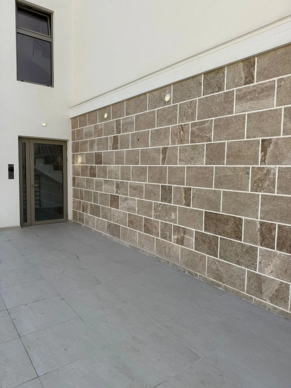 Facade of a modern residential building in Tivat, Montenegro: natural stone cladding, glass entrance area, and terrace.