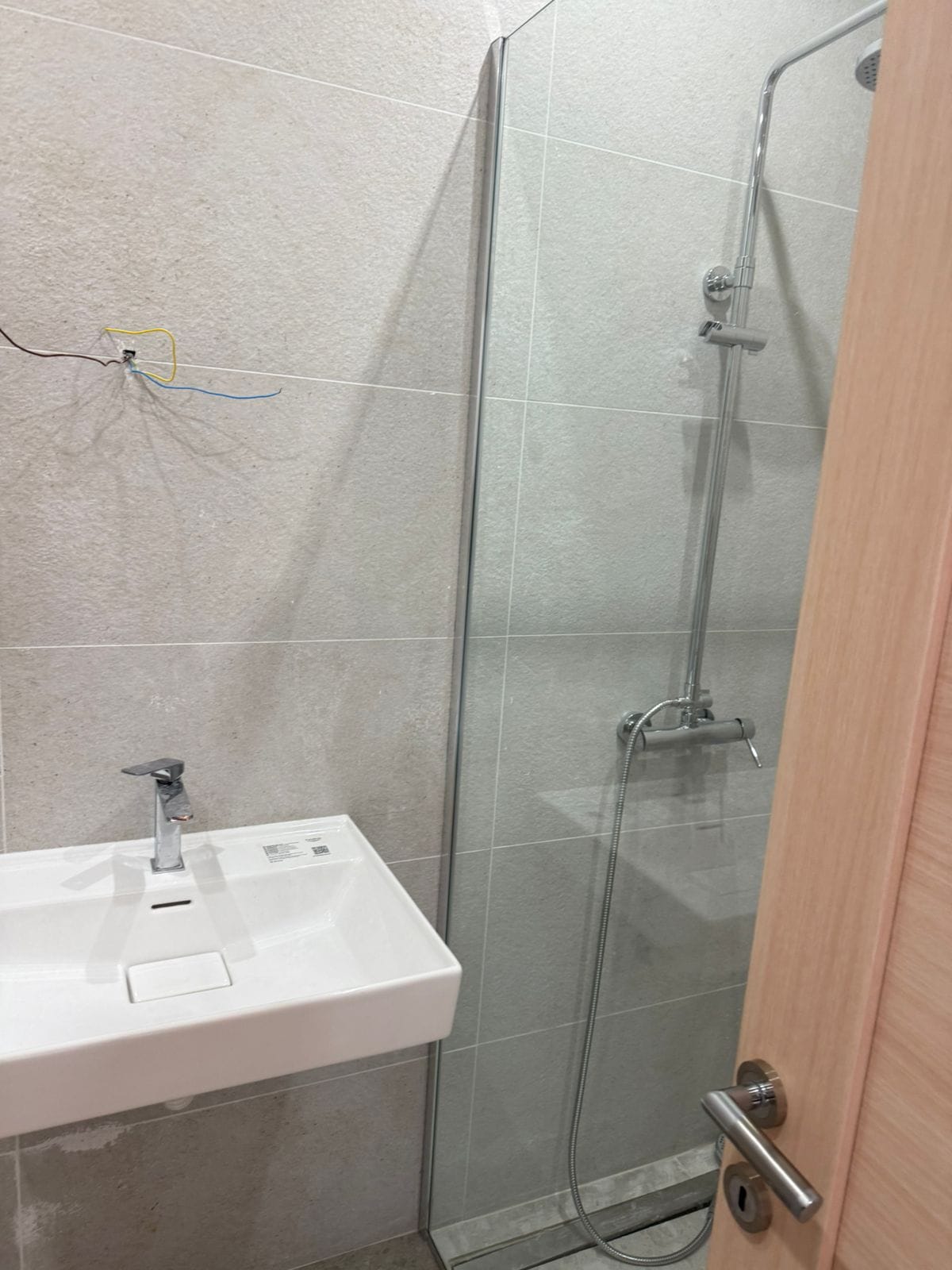 Modernes Badezimmer in einer Wohnung in Tivat, Montenegro: Duschkabine, weißes Waschbecken und Fliesenverkleidung.