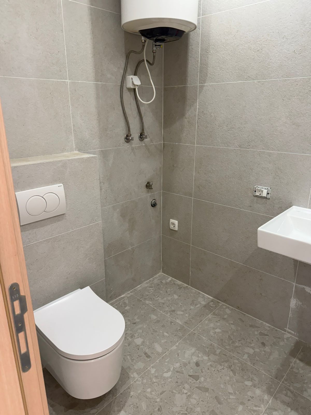 Modernes Badezimmer in einer Wohnung in Tivat, Montenegro: graue Fliesen, hängendes WC und Boiler.