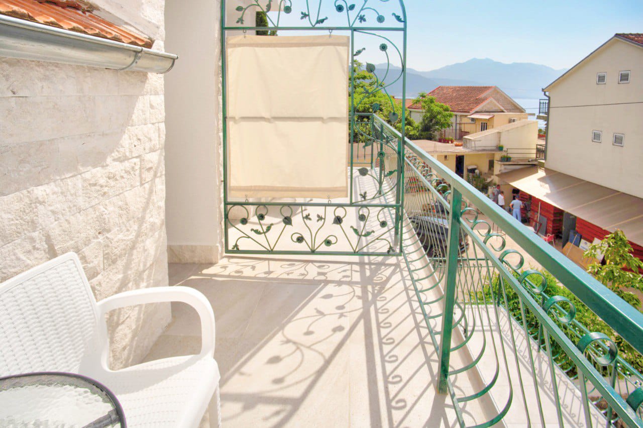 Balcony with wrought-iron railing and sea view in an apartment in Baošići, Montenegro. White furniture, stone wall finish.