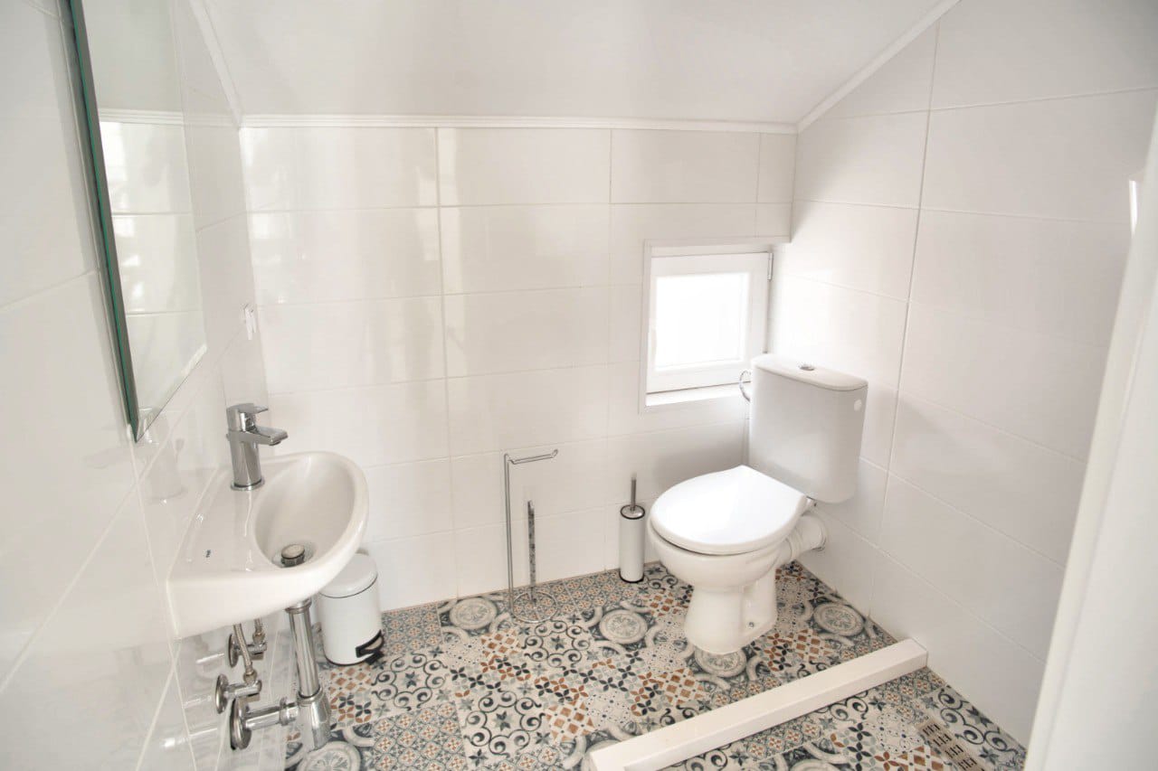 Bright bathroom with patterned tiles in a duplex, Baošići, Montenegro: fixtures, white finishes, and a window.