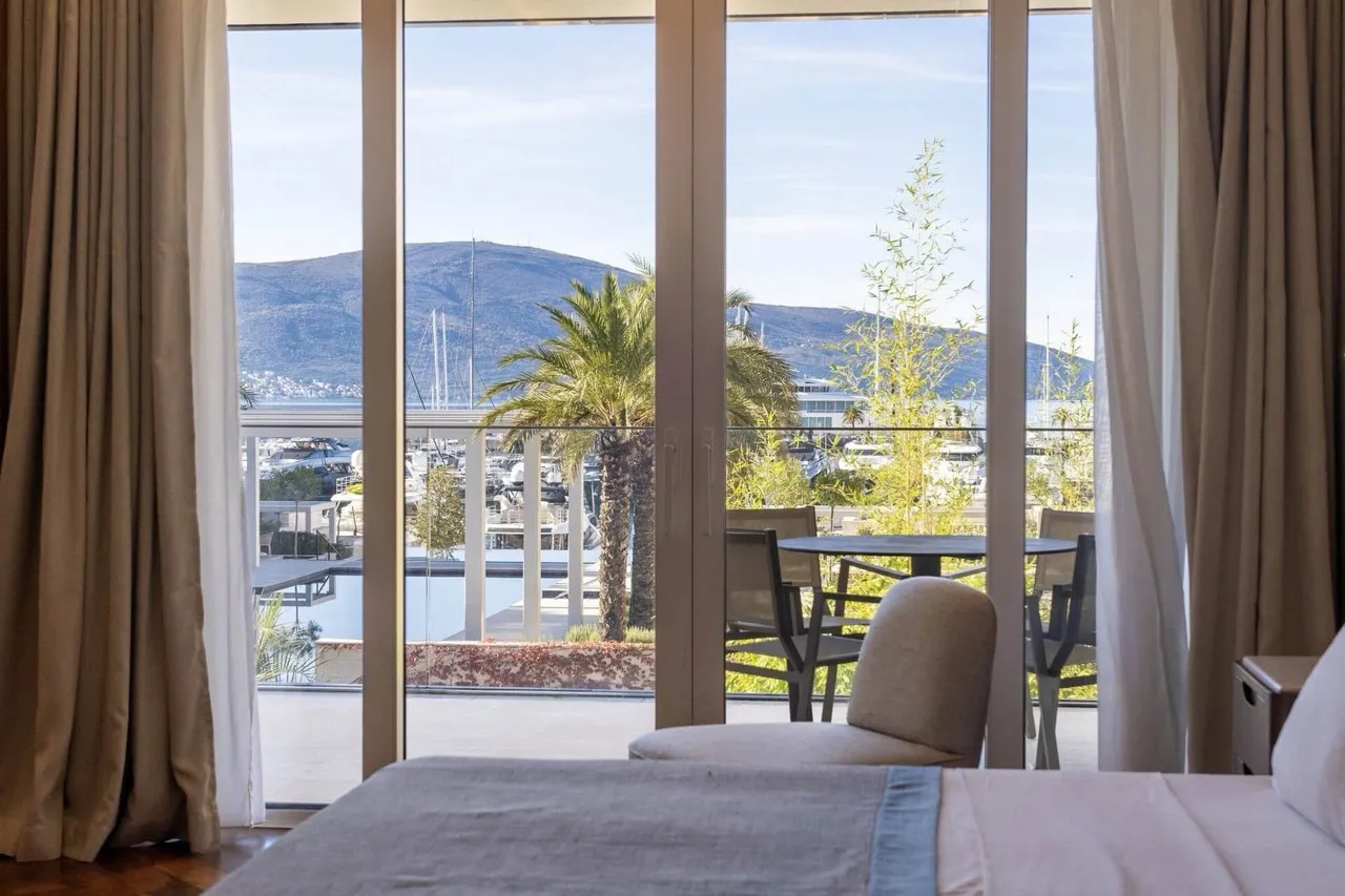 View from the bedroom of the marina and yachts in Porto Montenegro, Tivat, Montenegro: panoramic windows and a furnished terrace.