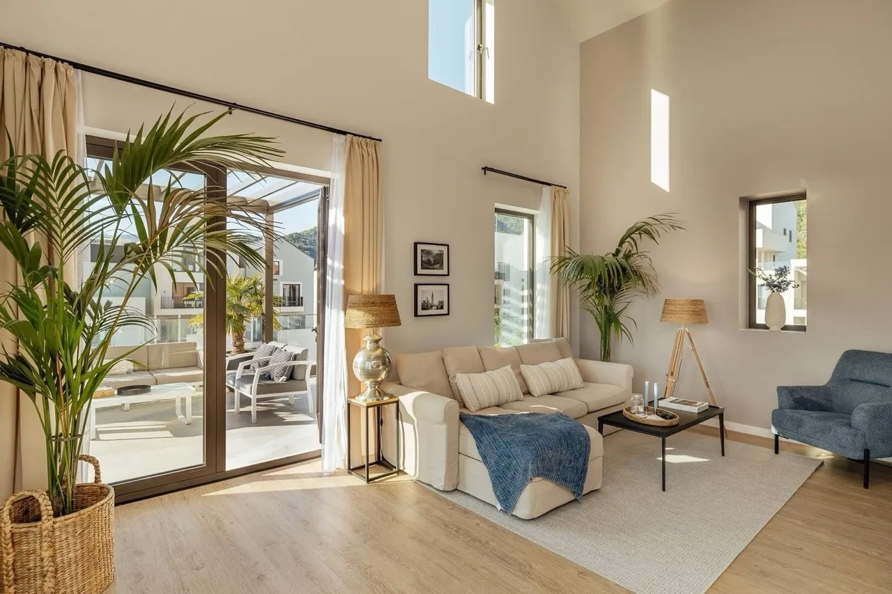 Geräumiges, modernes Wohnzimmer mit Sofa, Pflanzen und großen Schiebefenstern, die auf eine Terrasse führen.