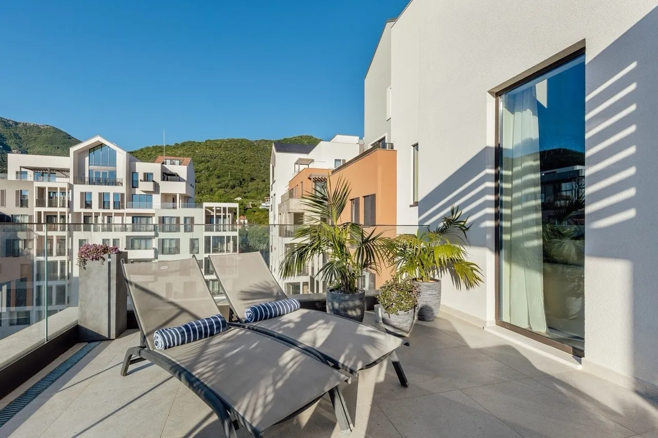Ein geräumiger Balkon mit zwei Sonnenliegen, Topfpflanzen sowie Berg- und Stadtblick.