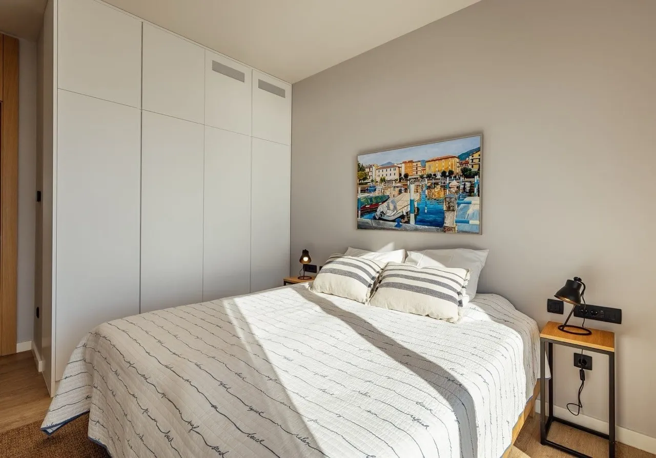 Ein helles Schlafzimmer mit weißem Bett, großem Kleiderschrank und Wandbild.