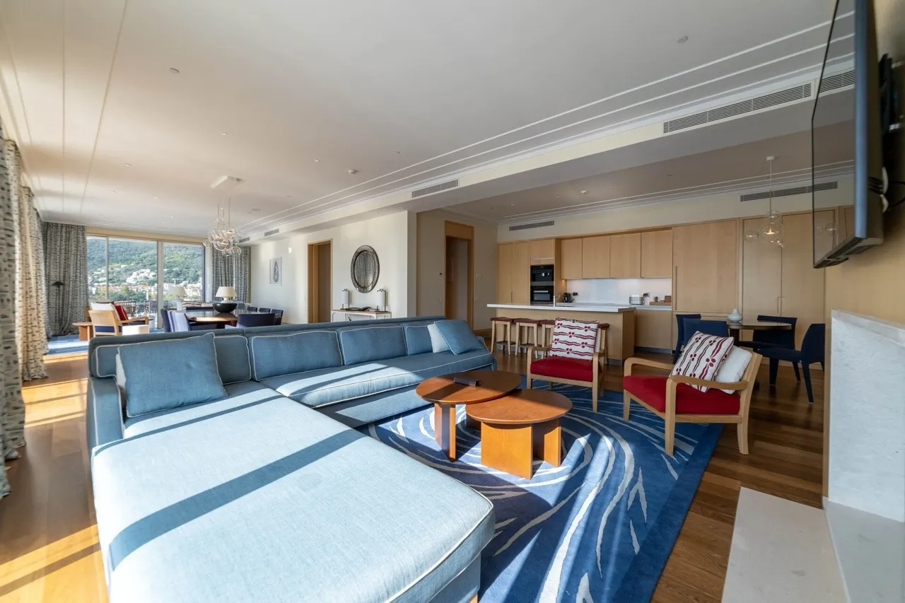 Geräumiges Wohnzimmer mit Küche in einer Wohnung in Tivat, Montenegro: blaues Sofa, Holzmöbel und Bergblick.