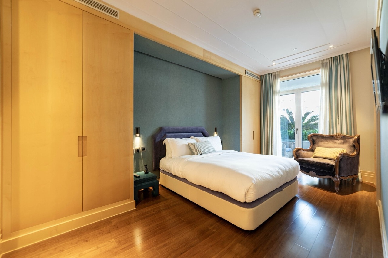 Spavaća soba u stanu Porto Montenegro, Tivat, Crna Gora: bračni krevet, drveni ormari i fotelja pored prozora.