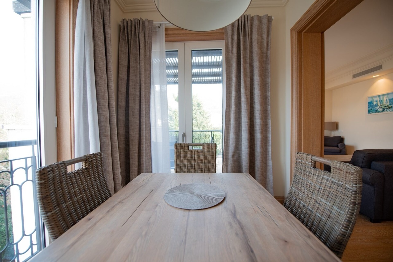 Trpezarijski deo sa drvenim stolom i pletenim stolicama u stanu Porto Montenegro, Tivat, Crna Gora.