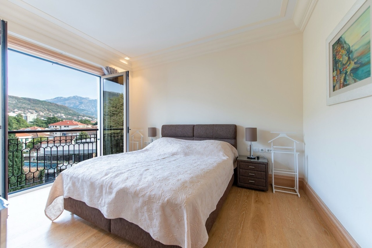 Spavaća soba u stanu u Porto Montenegru, Tivat, Crna Gora: bračni krevet, balkon s pogledom na planine i grad.