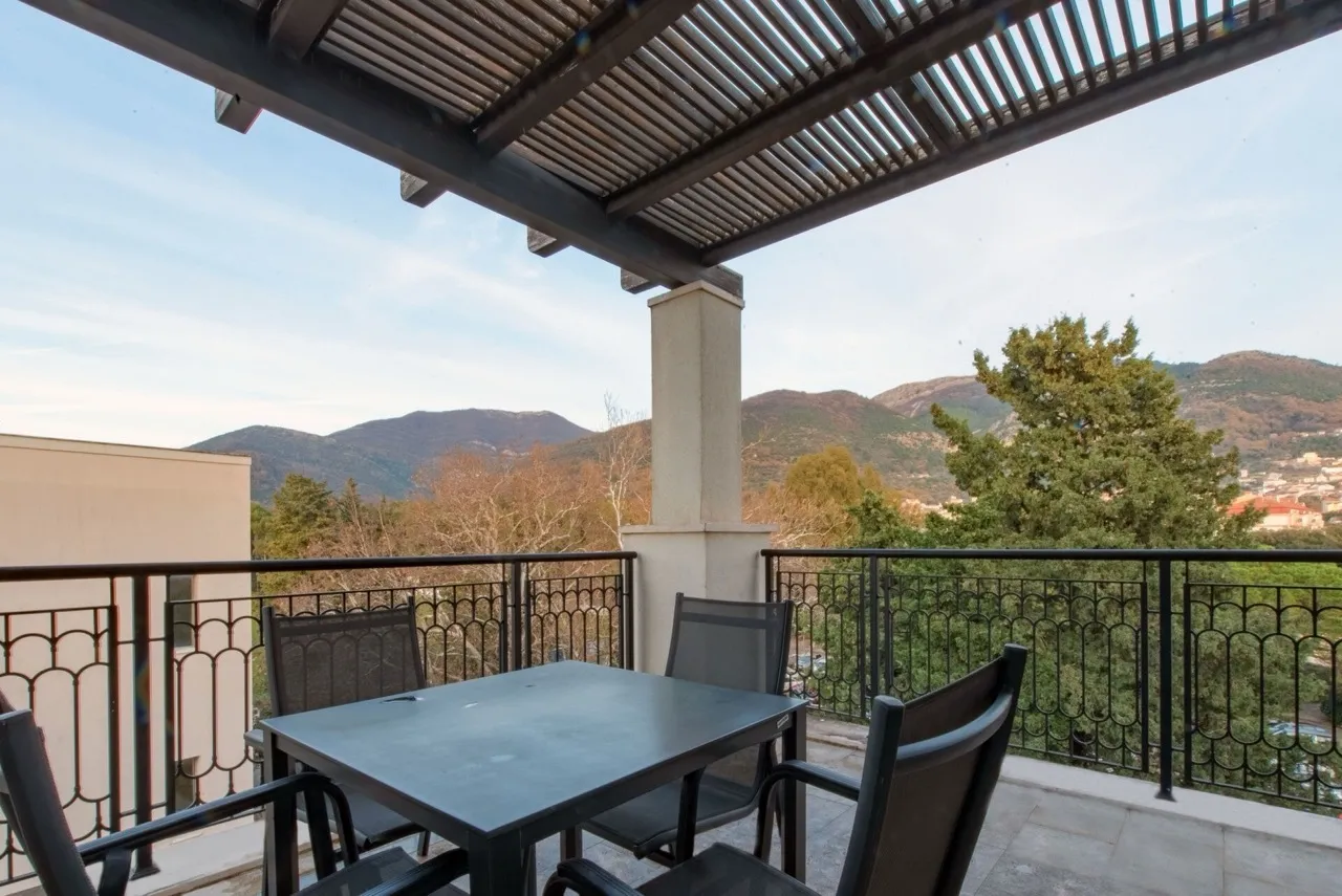 Terrasse mit Möbeln und Bergblick in einer Wohnung in Porto Montenegro, Tivat, Montenegro. Balkon mit Überdachung und schmiedeeisernem Geländer.
