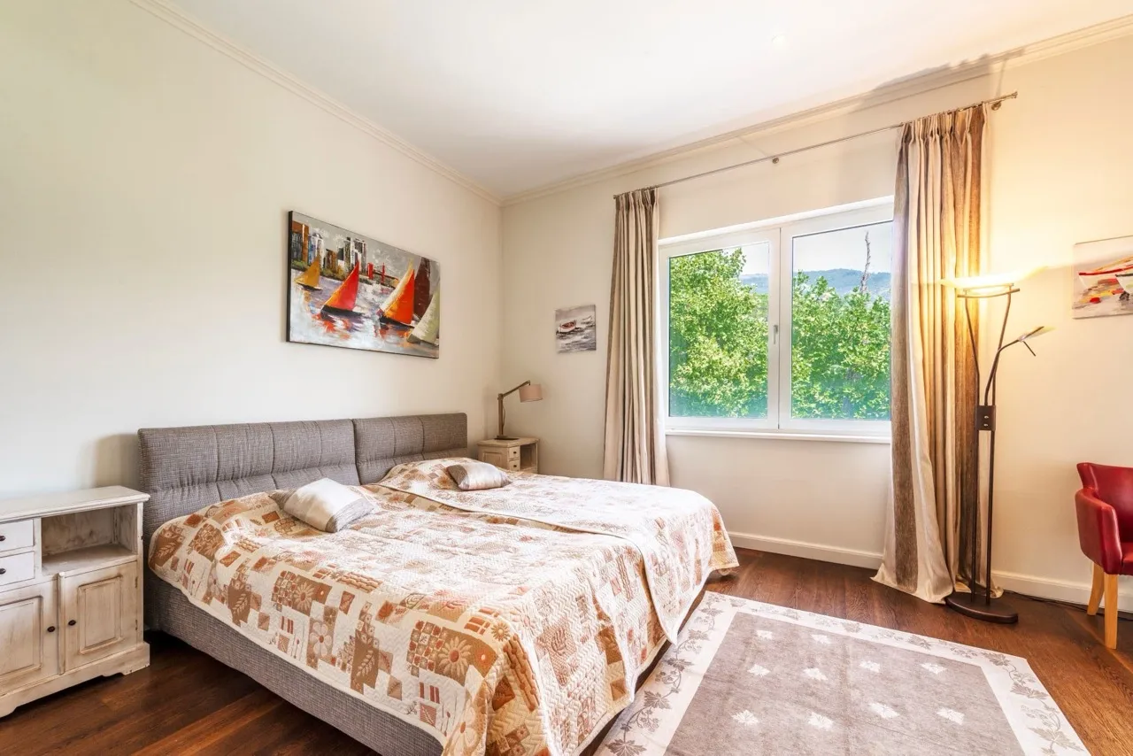 Gemütliches Schlafzimmer in einer Wohnung in Porto Montenegro, Tivat, Montenegro: Doppelbett, Parkett und Blick ins Grüne aus dem Fenster.