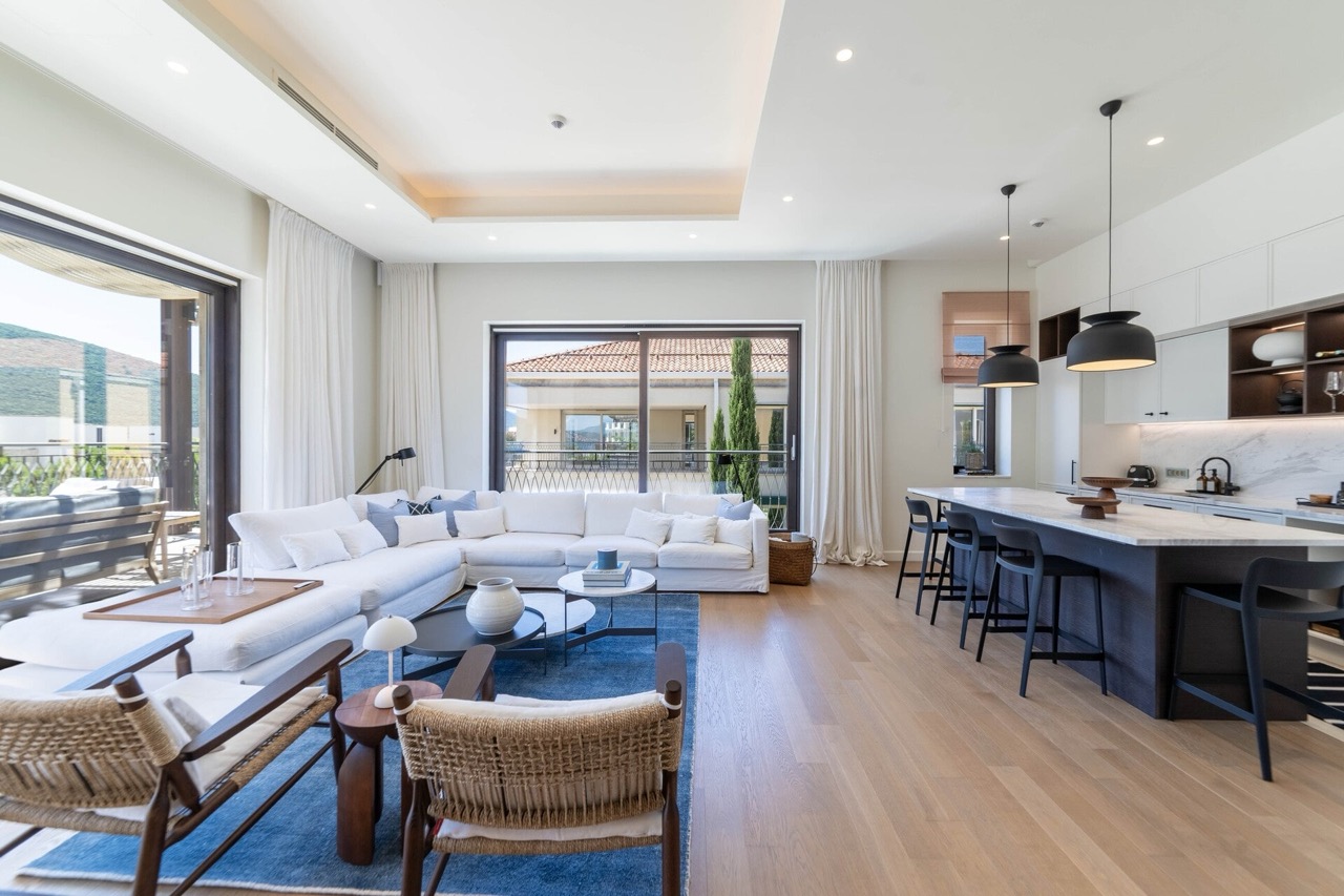 Modernes Wohnzimmer mit Küche in der Wohnung Portonovi, Kumbor, Montenegro: weißes Sofa, Kochinsel und Panoramafenster.