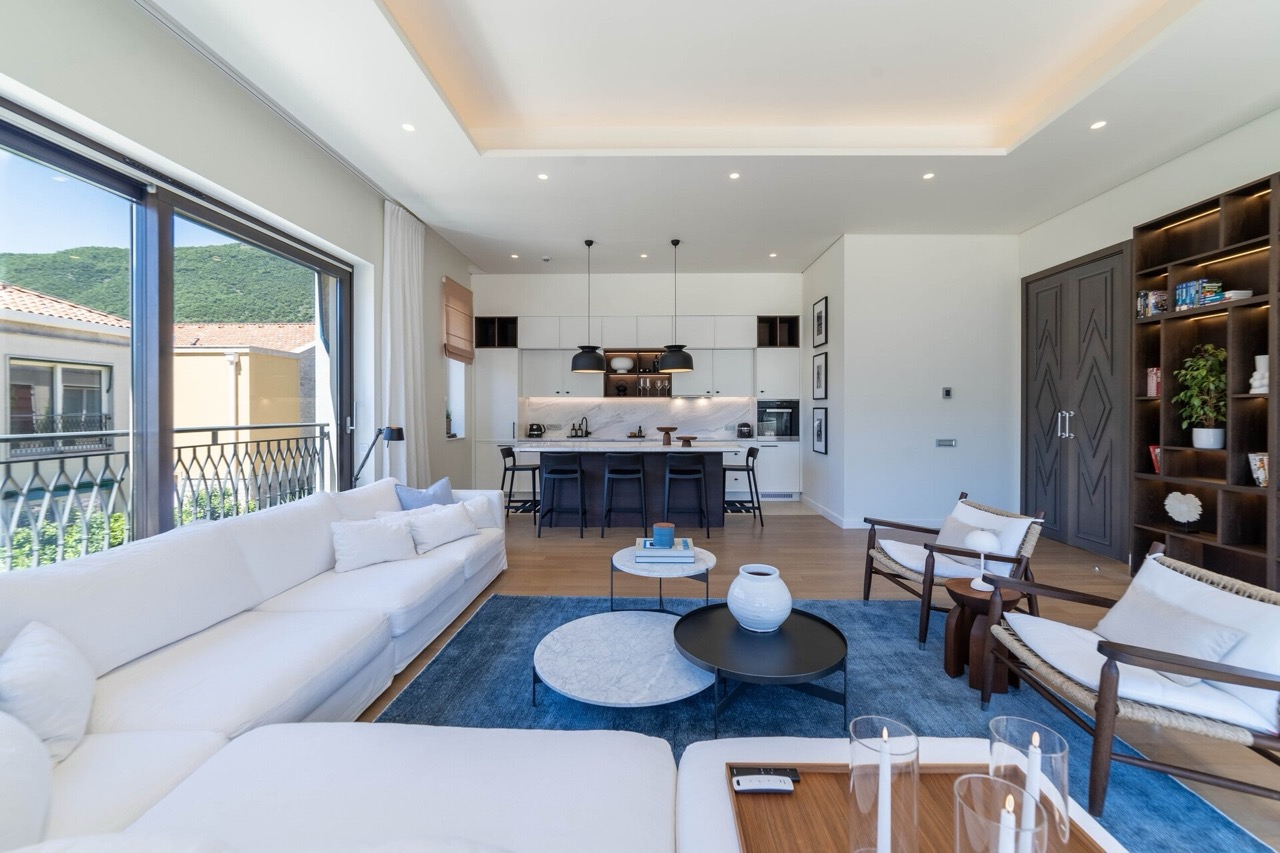 Modernes Wohnzimmer mit Küche in den Portonovi Apartments, Kumbor, Montenegro: weißes Sofa, Marmorinsel und Bergblick.