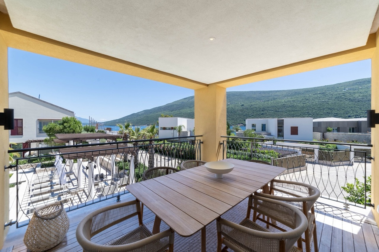 Terrasse mit Essbereich in der Wohnung Portonovi, Kumbor, Montenegro: Blick auf das Meer, die Berge und die moderne Wohnanlage.
