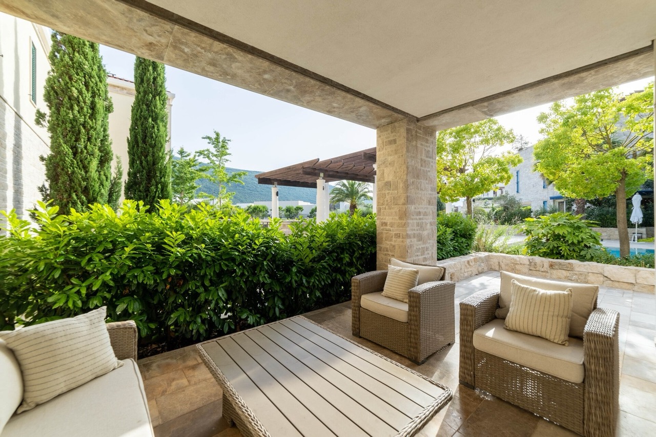 Gemütliche Terrasse mit Rattanmöbeln in einer Wohnung der Anlage Portonovi, Kumbor, Montenegro, mit Blick auf den Garten und die Berge.