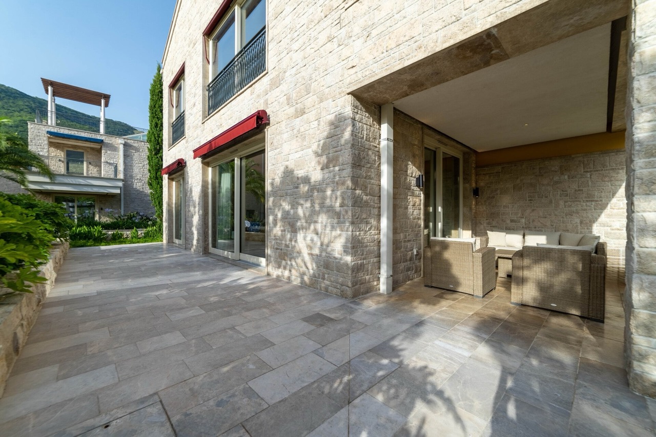 Terrasse einer Luxuswohnung in Portonovi, Kumbor, Montenegro: Steinverkleidung der Fassade, geflochtene Möbel und Bergblick.