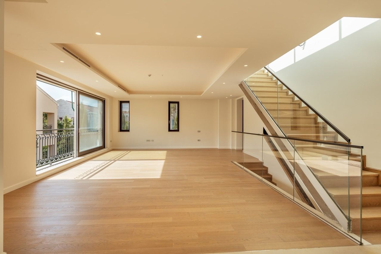 Spacious living room with wooden flooring and a staircase with glass railing in a villa in Kumbor, Montenegro.