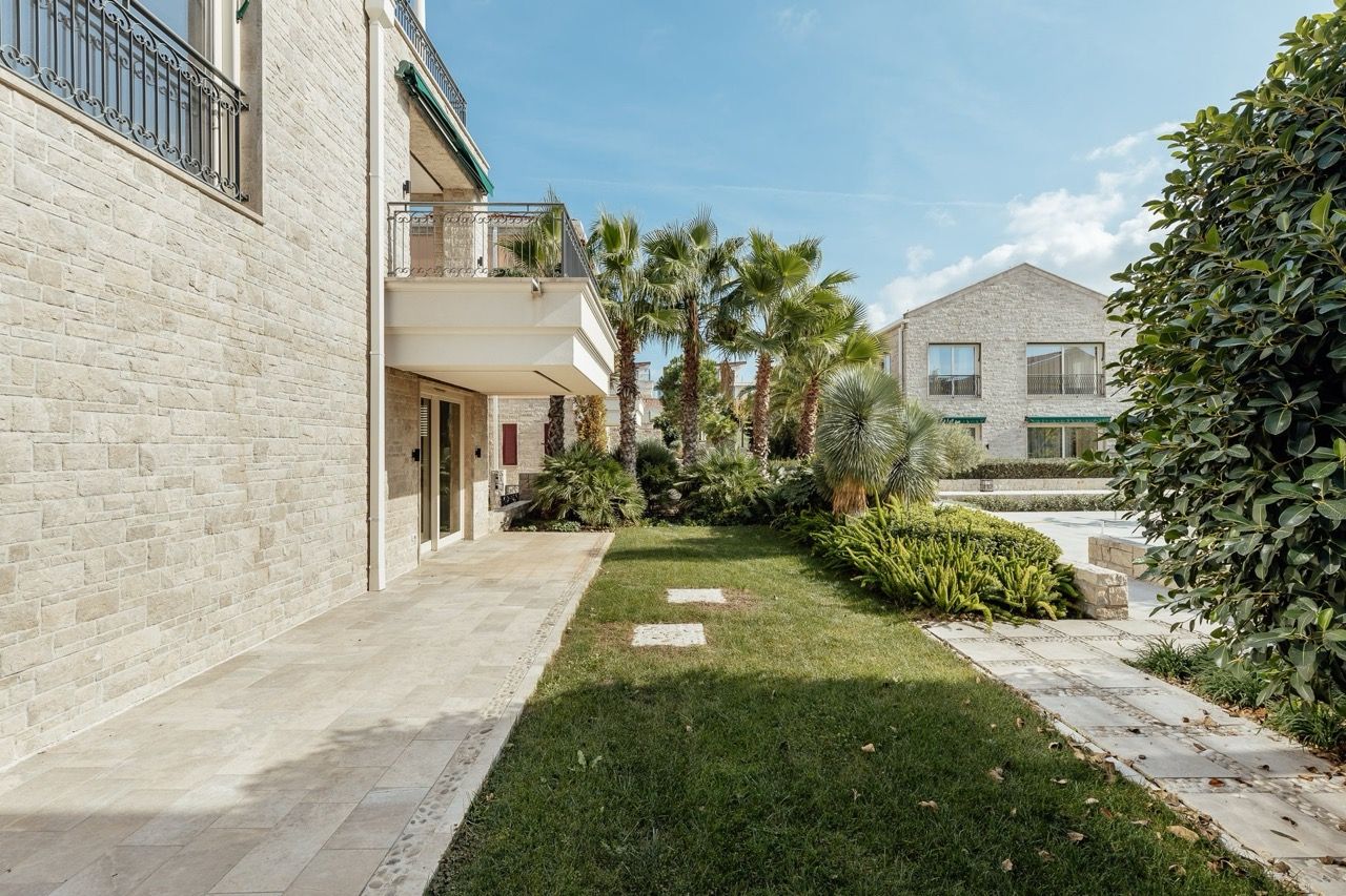 Villa in Portonovi, Kumbor, Montenegro: stone facade, terrace, well-kept garden with palm trees, and a view of the complex grounds.