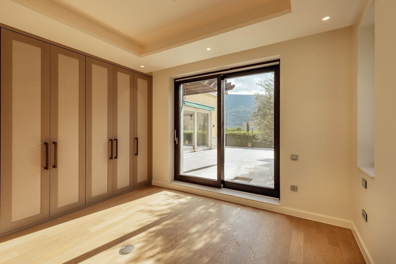 Bedroom with a panoramic window and built-in wardrobe in a villa in Kumbor, Montenegro, with access to the terrace and mountain views.