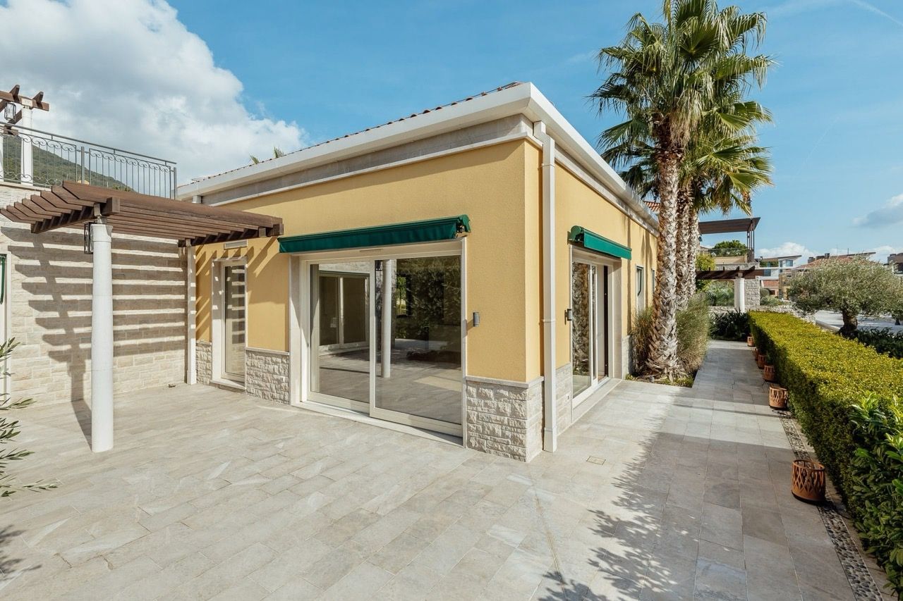 Modern villa in Portonovi, Kumbor, Montenegro: a terrace with stone finishes, panoramic windows, and palm trees in the garden.