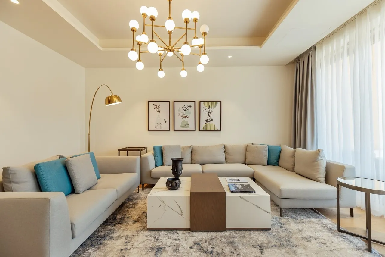 Nowoczesny salon w apartamencie Portonovi, Kumbor, Czarnogóra: jasne sofy, marmurowy stół i designerski żyrandol.
