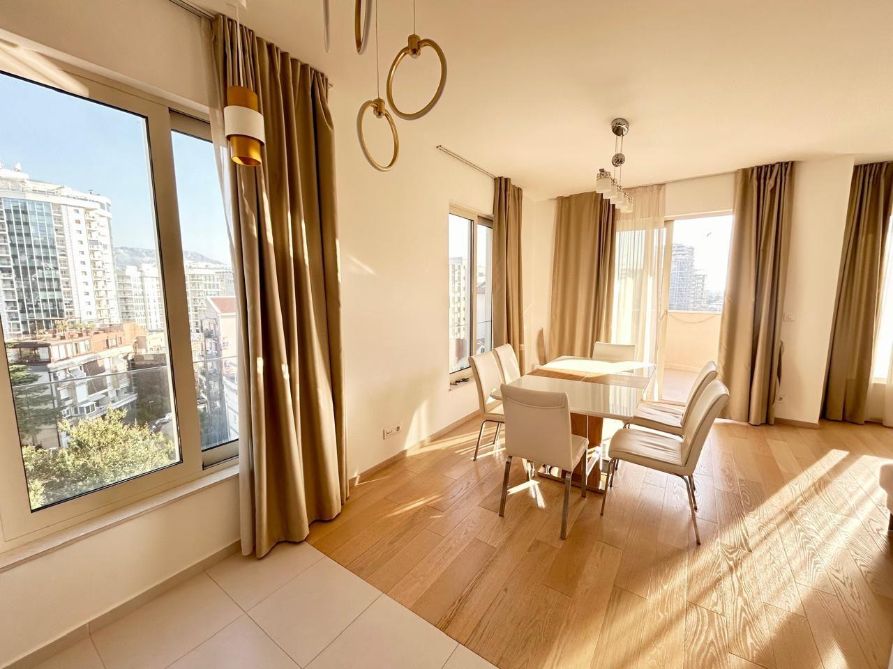 Savremeni dnevni boravak sa trpezarijom u stanu u Budvi, Crna Gora: panoramski prozori, svetao nameštaj i parket.