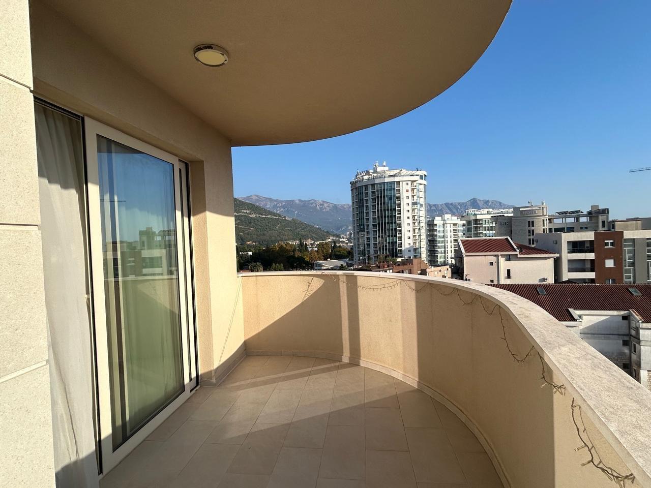 Prostran balkon s panoramskim pogledom na planine i grad Budvu, Crna Gora, u modernom stanu s panoramskim prozorima.