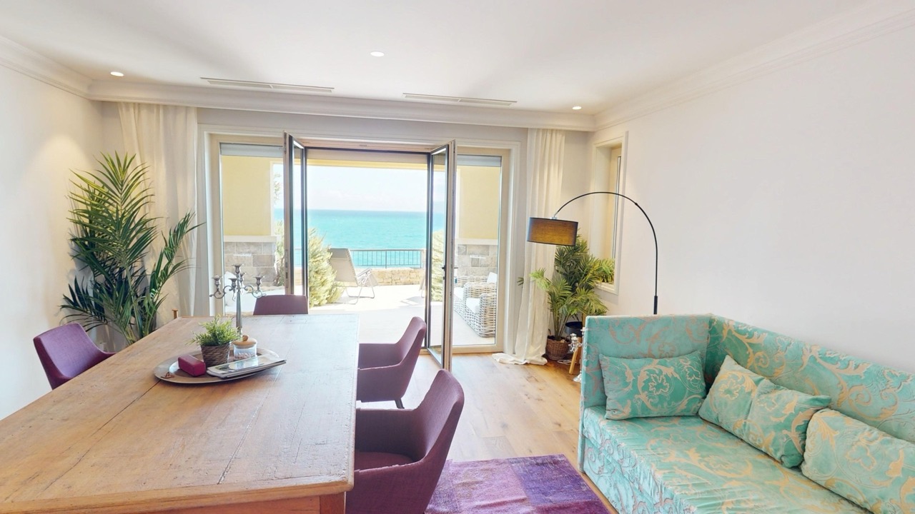 Wohnzimmer mit Meerblick in der Wohnung Luštica Bay, Radovići, Montenegro: Holztisch, türkisfarbenes Sofa und Terrasse.